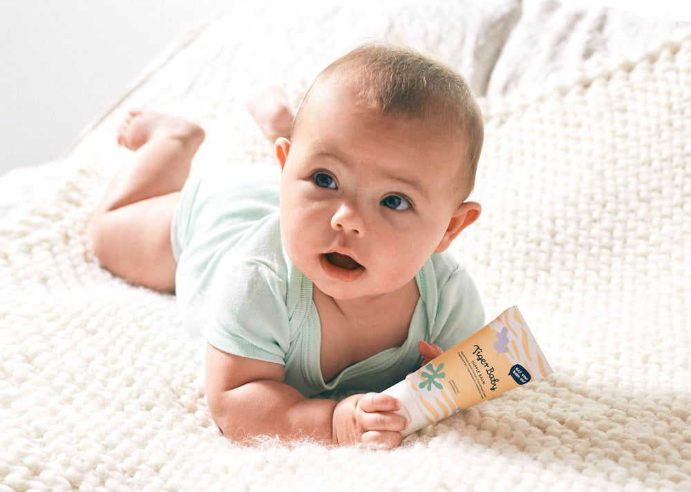 Image of baby holding a tube of Nipple Balm